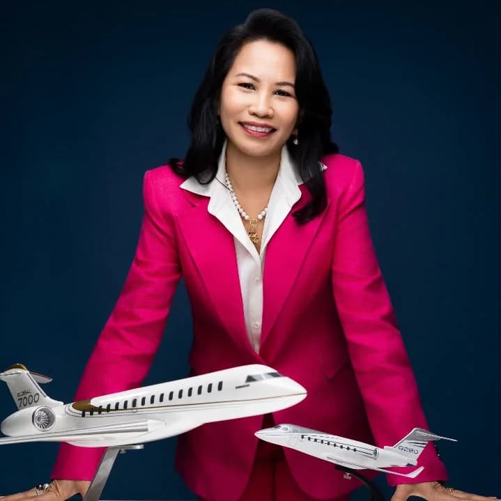 Aida Ismail in a pink jacket, leaning on a table with two business jet models in front of her